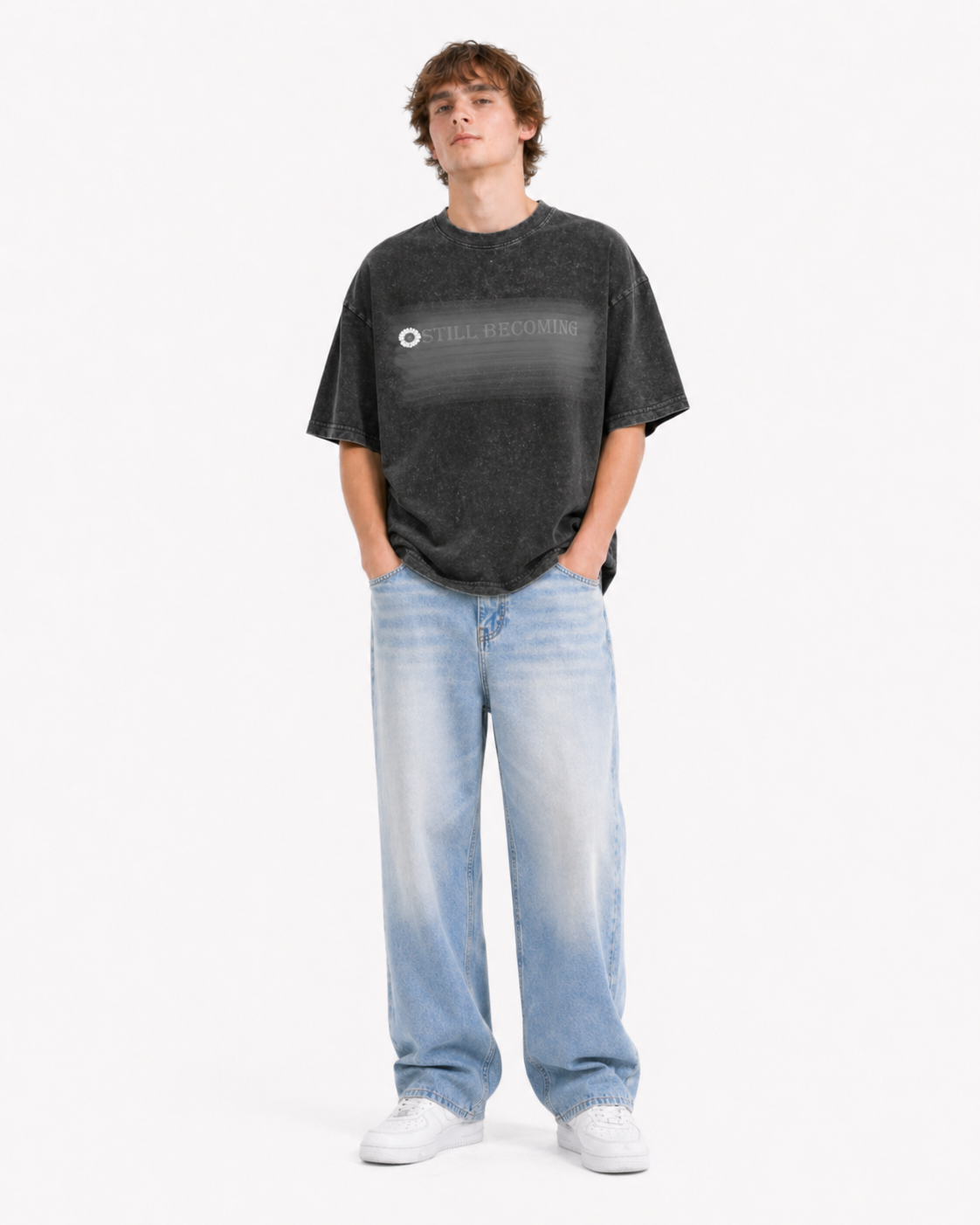 Model in acid-wash black tee with STILL BECOMING text, light blue wide-leg jeans, white sneakers
